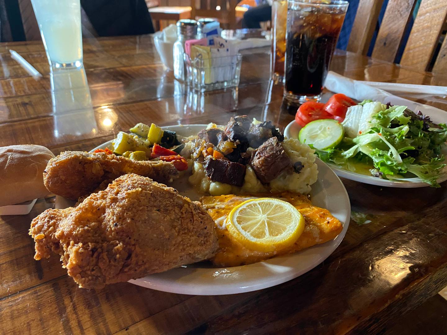 A salad and dinner roll sit beside a plate including fried chicken, oven-roasted vegetables, mashed potatoes topped with pot roast and a citrus salmon fillet, all on the Sunday brunch buffet at Starved Rock Lodge.