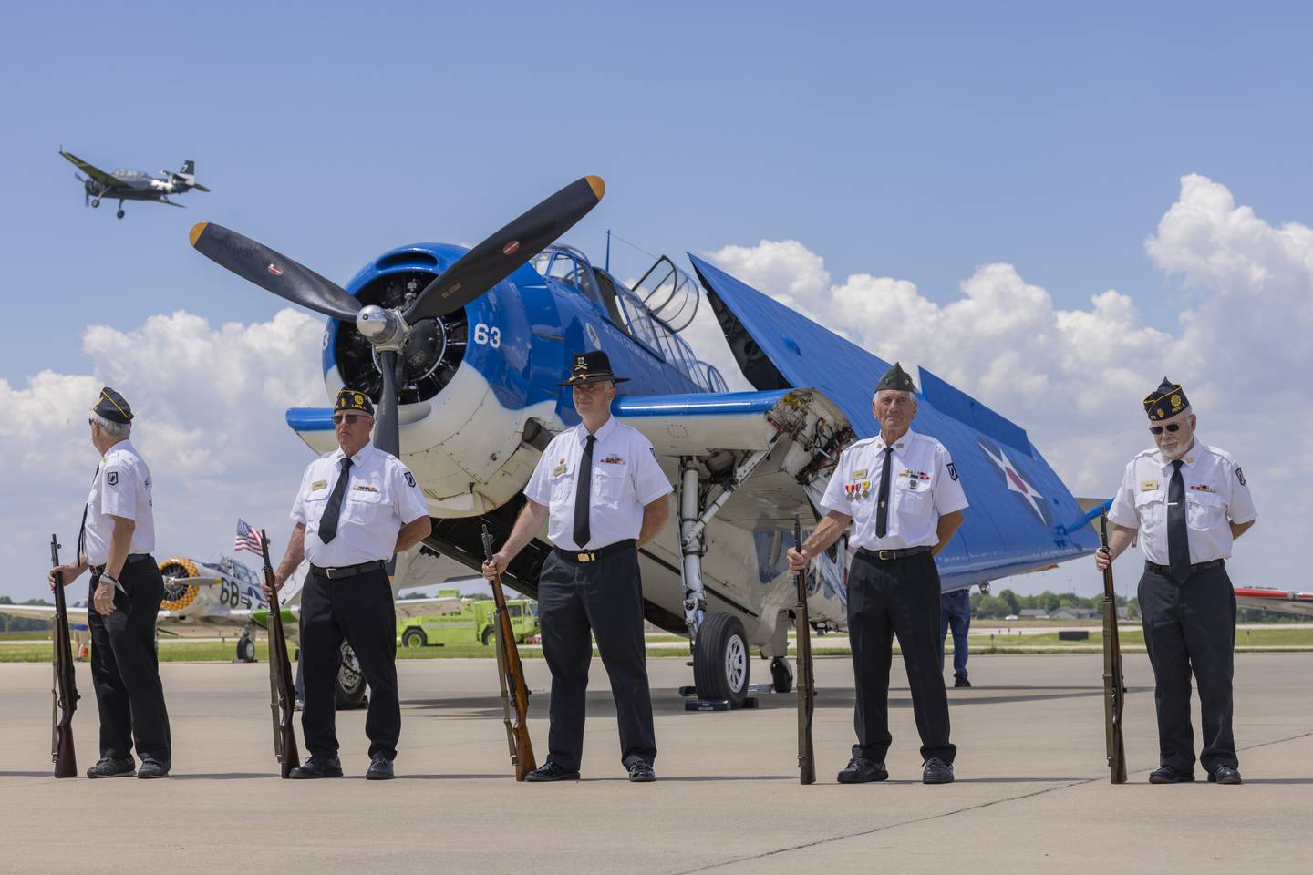 A TBM avenger containing folded flags takes off as the Peru Veterans Memorial Honor Guard prepares for a twenty one gun salute in honor to the fallen veterans during the TBM Avenger Reunion and Salute To The Veterans at Illinois Valley Regional Airport on May 18, 2024.
